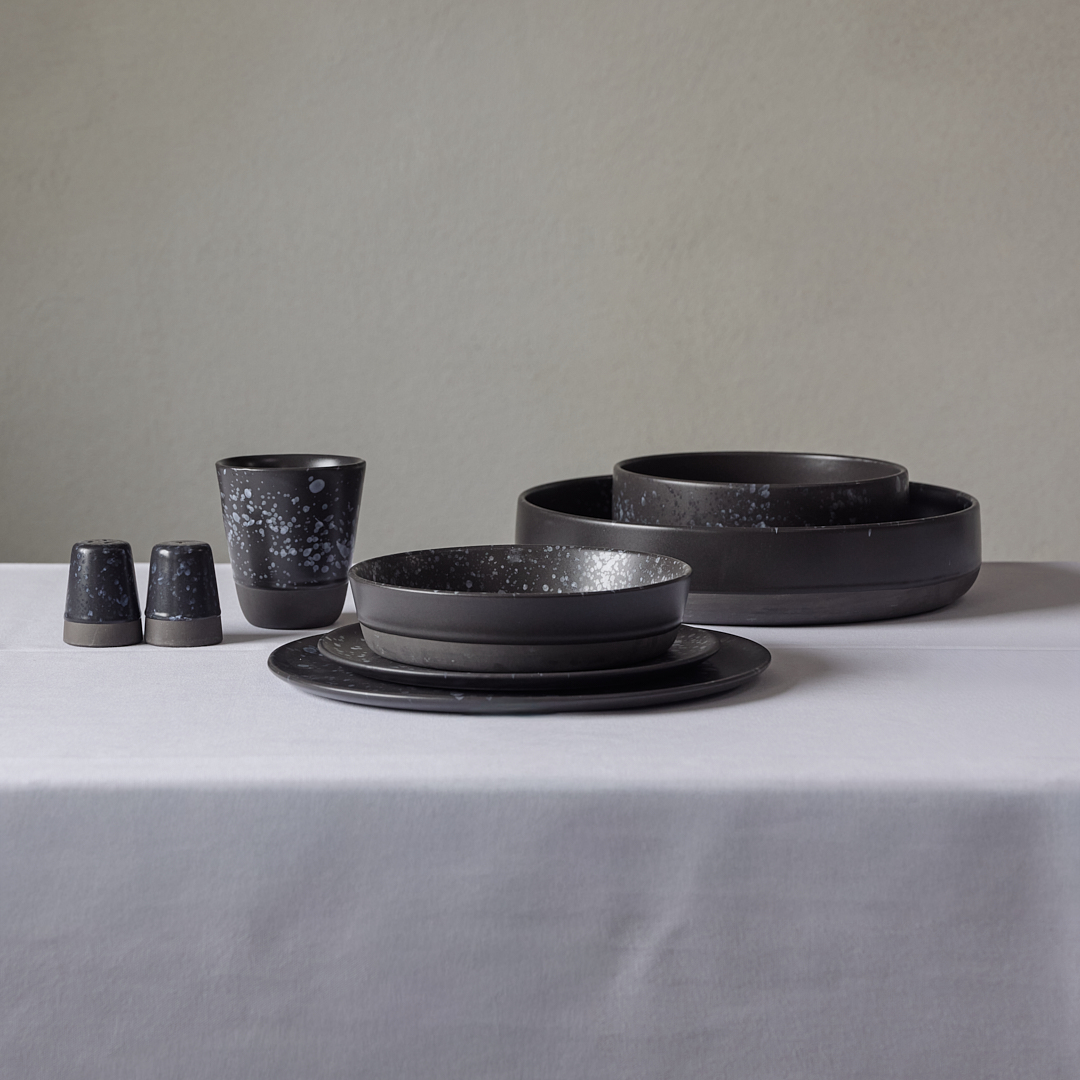 Eight shirts arranged on table in black, olive, grey, blue, white, red, mustard, and green.
